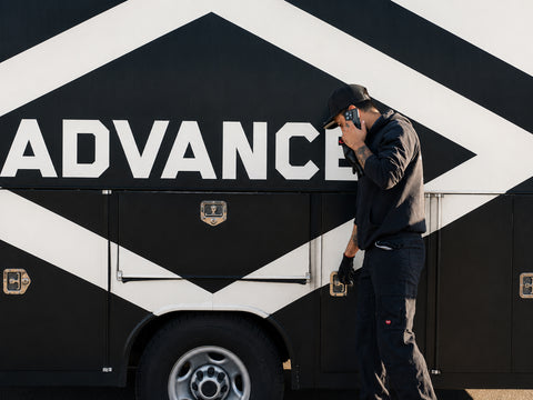 Advanced Air & Vacuum automotive service technician on a phone beside the company service trailer for field support.