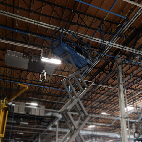 Technician installing Prevost aluminum compressed air piping system overhead using scissor lift in industrial facility in Southern California