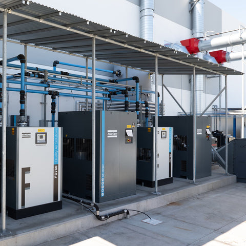 Atlas Copco rotary screw compressor system installation with multiple compressors and air distribution piping in industrial facility
