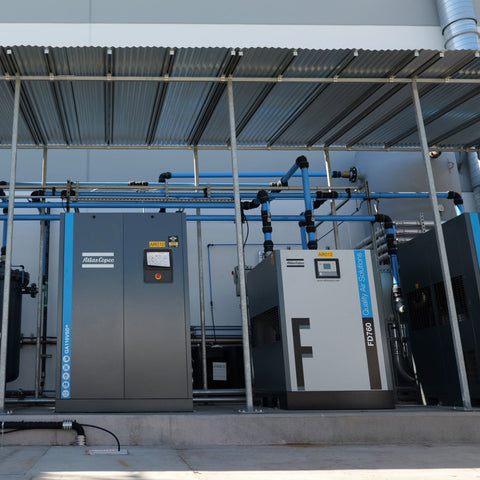 Atlas Copco rotary screw compressor system installation with multiple compressors and air distribution piping in industrial facility