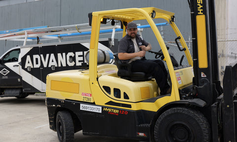 Advanced Air & Vacuum compressor installer on forklift at job with Advanced truck in background.